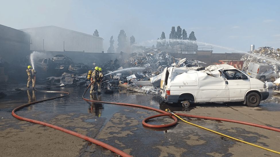 firefighters spray water on the scrapyard
