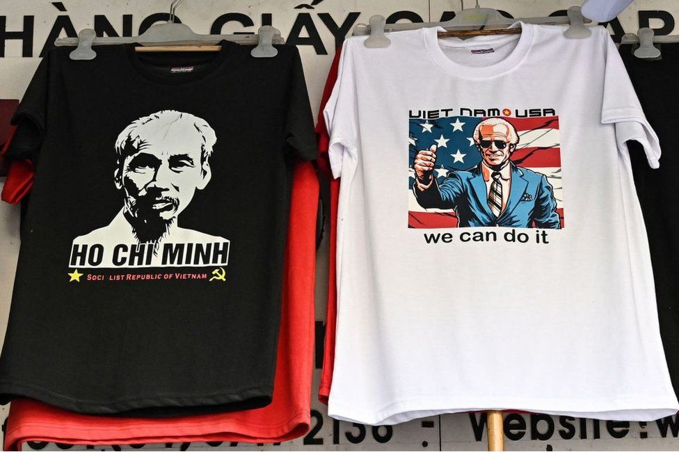 An employee installs a t-shirt with an image of photo of US President Joe Biden next to another one showing a portrait Vietnamese late President Ho Chi Minh in a souvenir shop