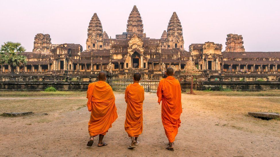 Three people walk towards the Angkor Wat temple complex