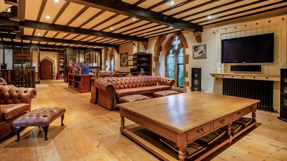 Large reception room with red sofas, large fireplace, church windows and a large wooden door