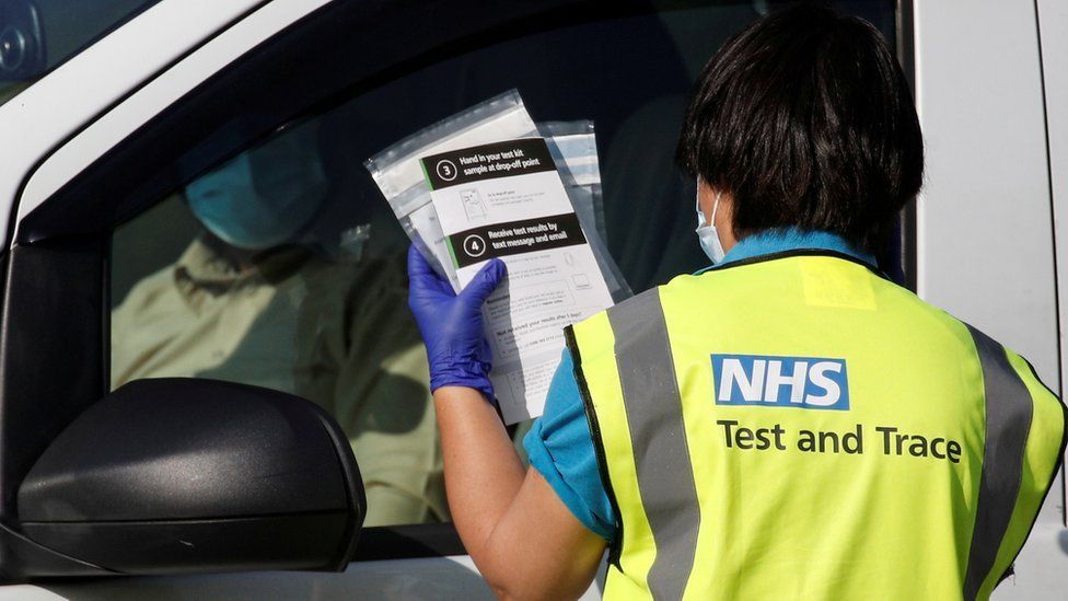 An NHS test and trace worker takes a coronavirus test to someone waiting in a vehicle