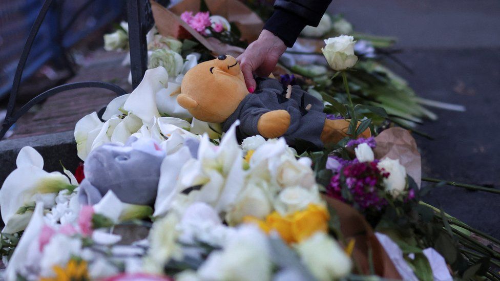 A woman leaves a teddy bear outside a school in Belgrade following a mass shooting