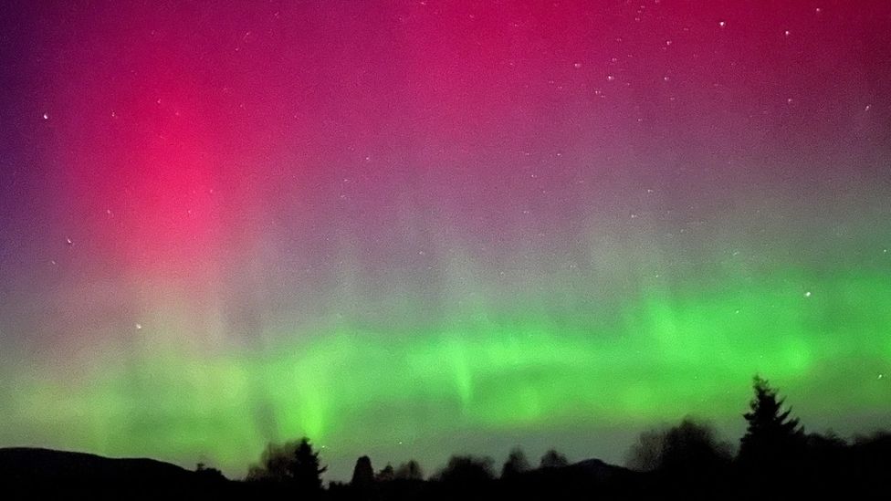 Bright green and deep red colours fill the sky in the Scottish Highlands