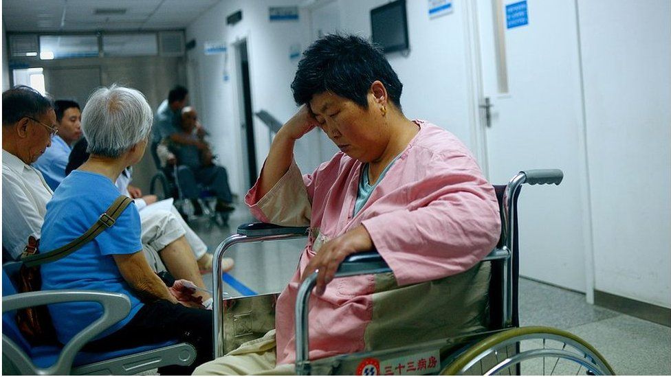 A woman (C) siting on a wheelchair waits for a health check outside a consulting room a hospital in Beijing on 3 July 2014