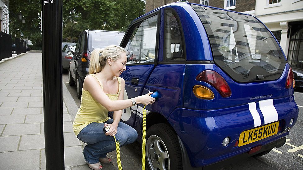 A woman charges a tiny electric car at a street charging point