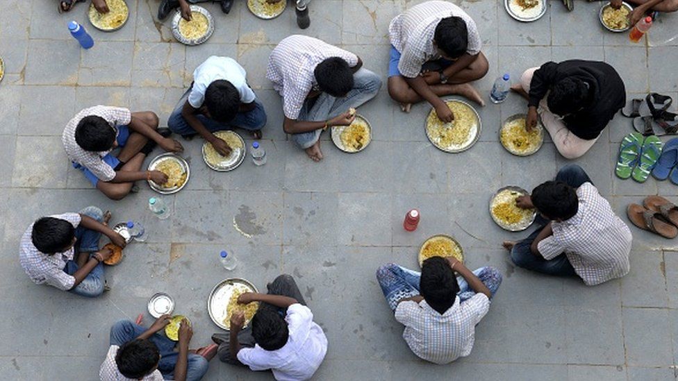 Учащиеся едят в середине дня во время обеденного перерыва в государственной средней школе на окраине Хайдарабада