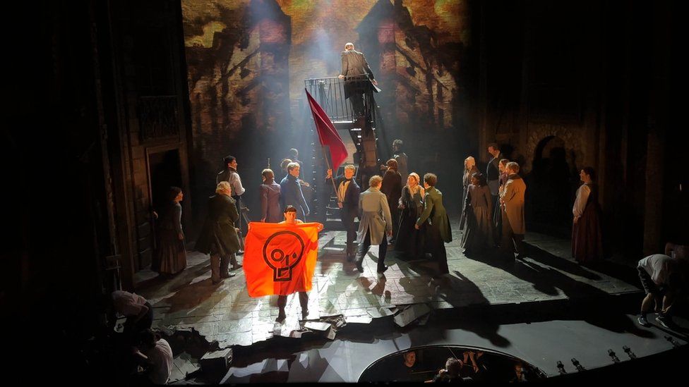 A Just Stop Oil protester holds up an orange banner after disrupting a performance of Les Miserables