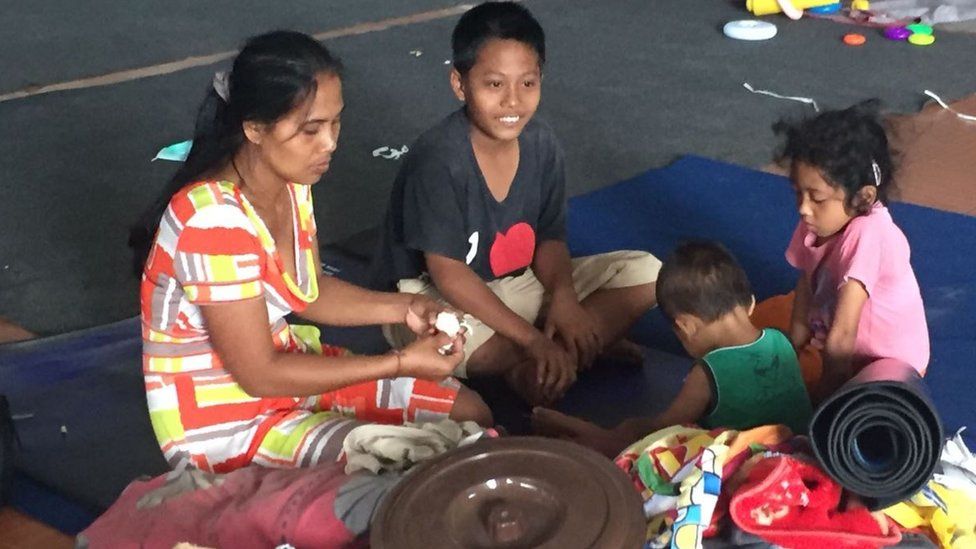 Ketut Seri and her young family are pictured sitting on the floor of a center