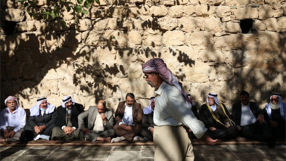 Men sit against a wall in Lalish ahead of the inauguration ceremony for the new Yazidi spiritual leader