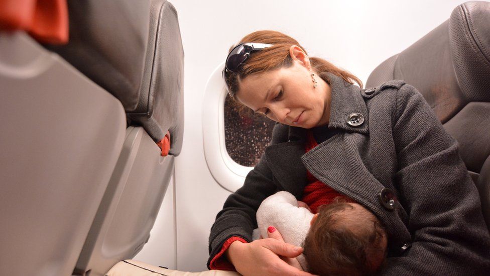 A woman breastfeeds her baby on an aeroplane