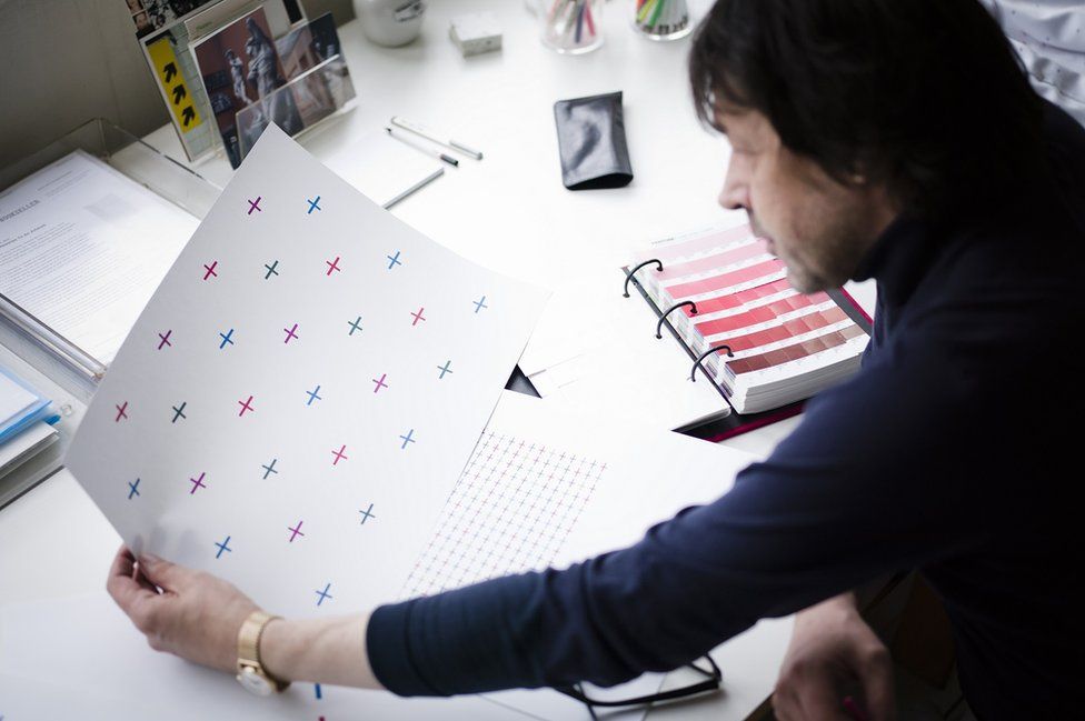 Peter Saville CBE looking at the multicoloured cross pattern on a sheet of paper
