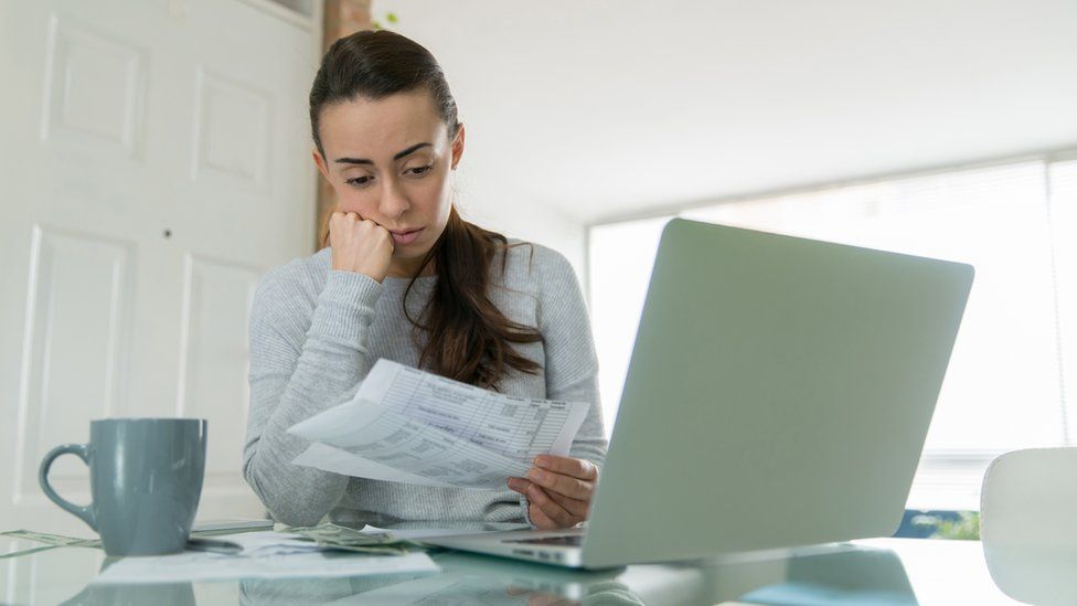 A stock photo of a woman looking worried holding bills