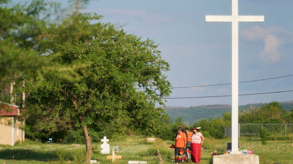 Women walk in a field where human remains were discovered in unmarked graves at the site of the former Marieval Indian Residential School on the Cowessess First Nation in Saskatchewan