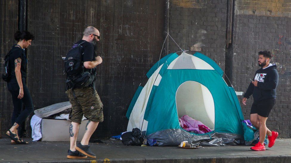 People walk past homeless person's tent in London in September