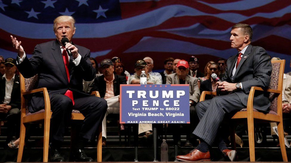 Donald Trump and General Flynn sit on stage in front of an audience during an election rally
