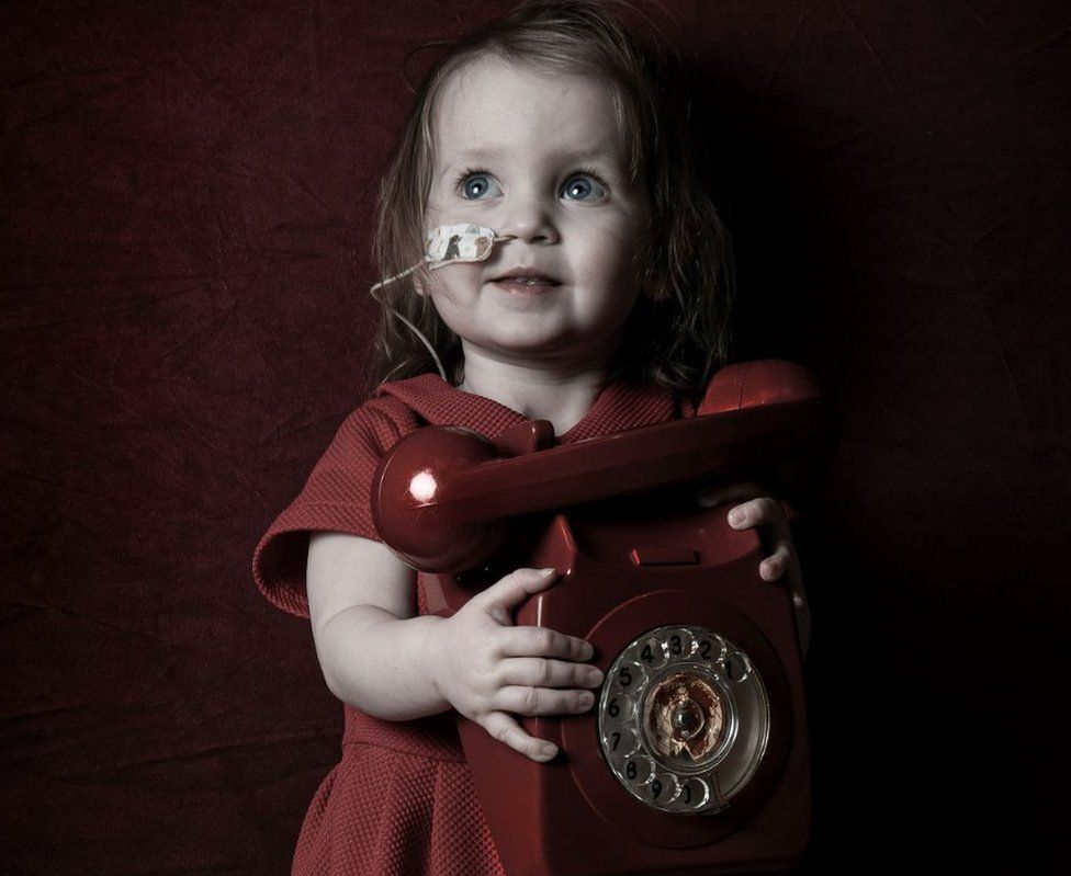 A young girl holds a red phone