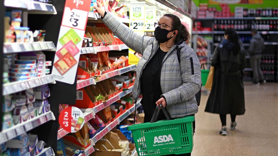 A shopper wearing a face mask chooses items off the shelves of an Asda supermarket