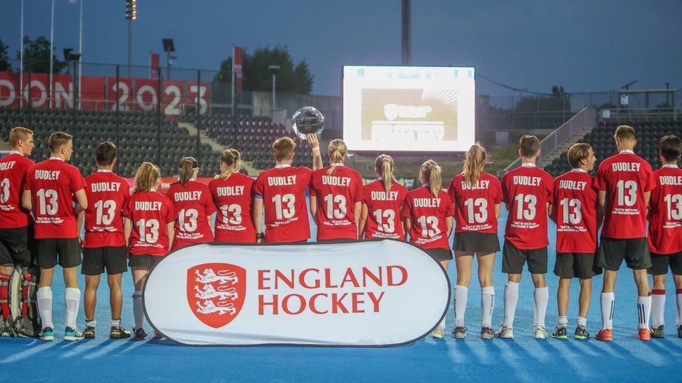 Hockey players wearing red and black kit with the name 'Dudley' and number '13' printed on the backs