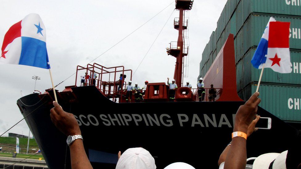 A person hold Panama flags in front of a ship docked in the Panama canal