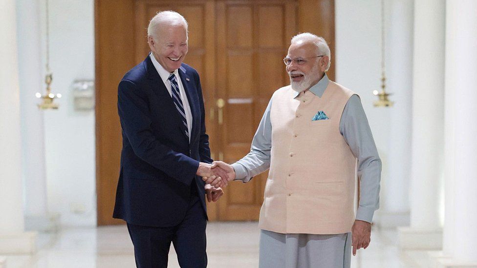 Премьер-министр Индии Нарендра Моди принимает президента США Джо Байдена (слева) в Нью-Дели, Индия. Двое мужчин смеются и пожимают друг другу руки.