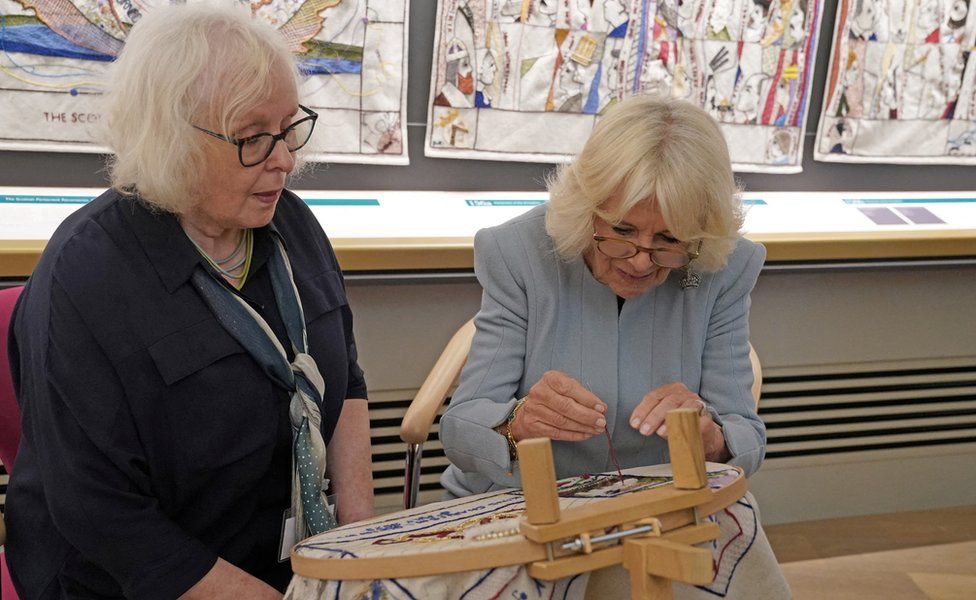 Queen Camilla adds the final stitches on a new panel for the tapestry