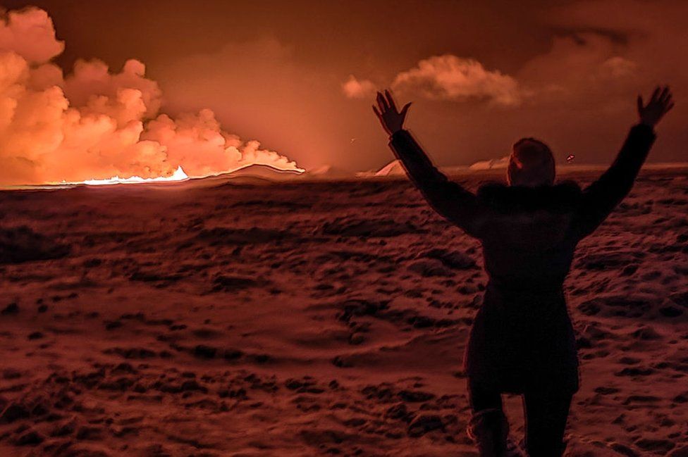 A local resident watch smoke billow as the lava colour the night sky orange from an volcanic eruption on the Reykjanes peninsula 3 km north of Grindavik, western Iceland on December 18, 2023.