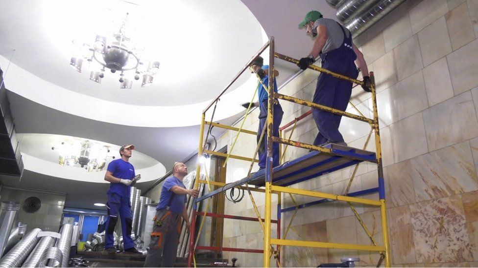 Workers in blue overalls stand on scaffolding in a metro station in Kharkiv