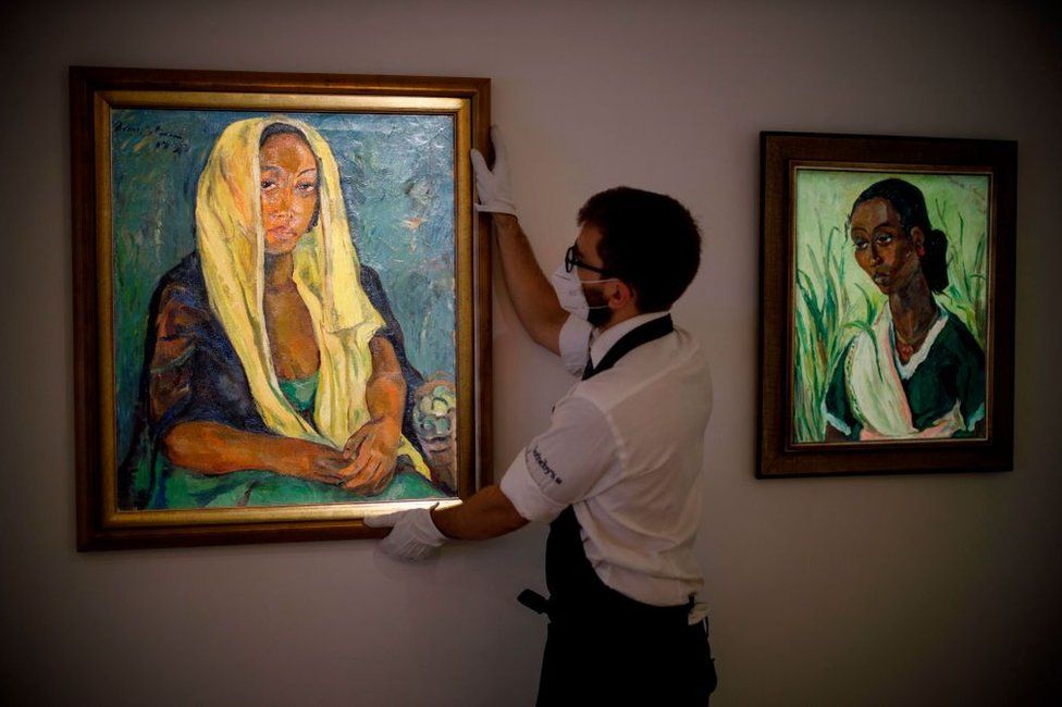 A gallery worker poses with an artwork entitled The Yellow Shawl (L) alongside The Green Sari (R) by South African artist Irma Stern.
