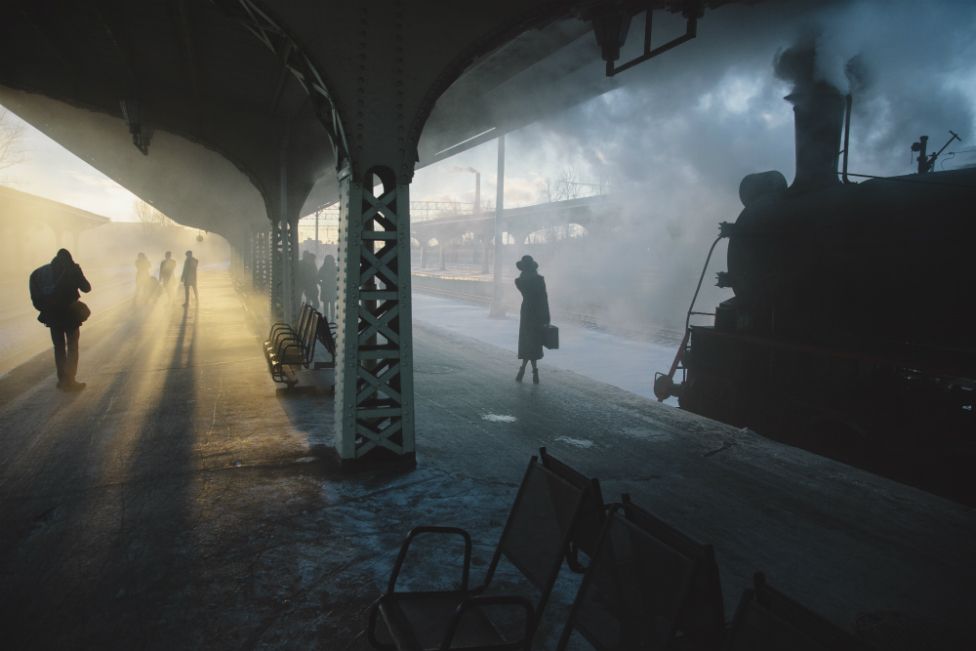 Passengers stand on a train platform in the early morning