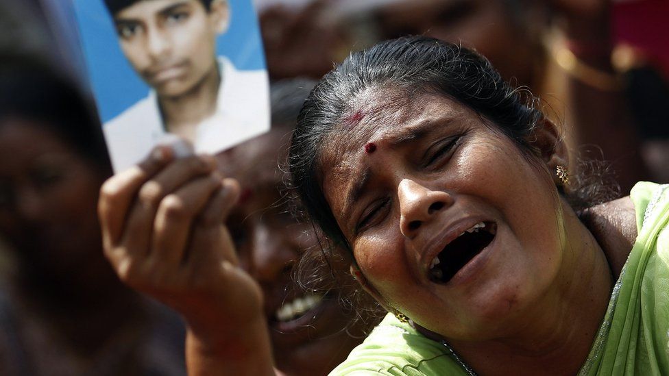Тамильская женщина плачет, держа изображение пропавшего члена семьи во время войны
