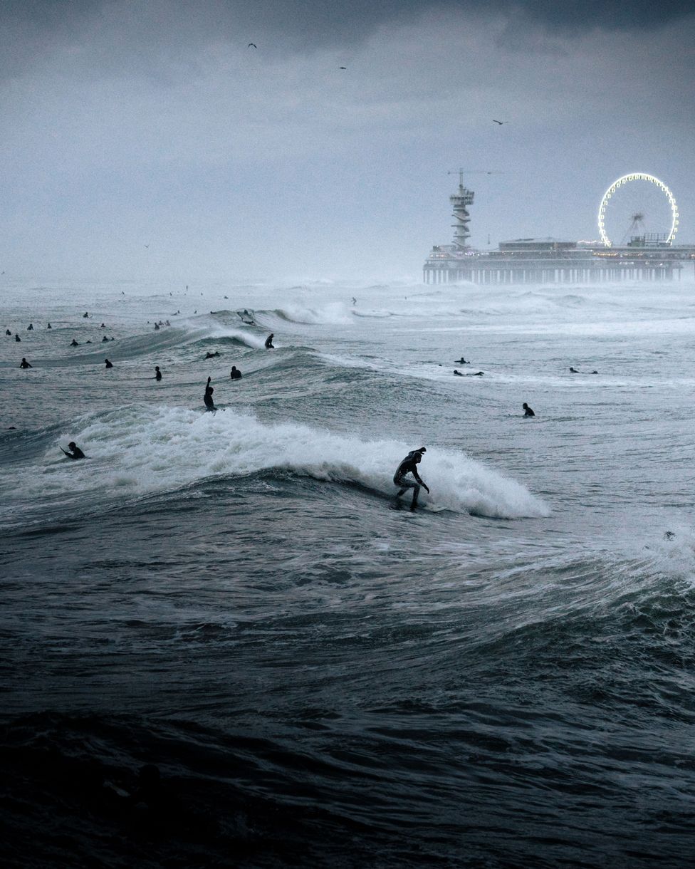 People surfing at sea with a pier visible in the distance