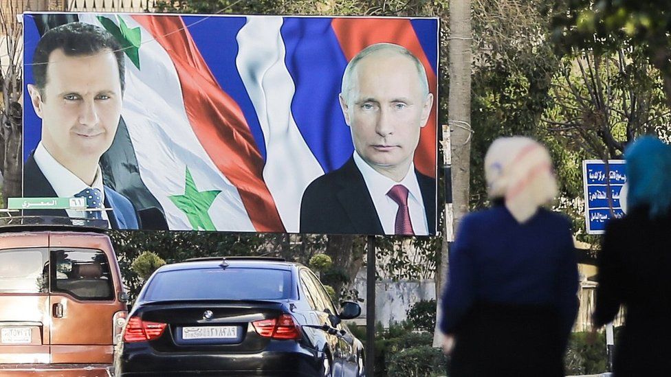 Сирийские женщины проходят мимо гигантского плаката с изображением президента Башара аль-Асада (слева) и его российского коллеги Владимира Путина (справа) в Алеппо (9 марта 2017 г.)