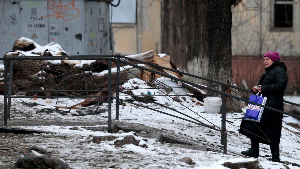 Woman struggling with bag on ground damaged by missile strike on 5 December in snow.