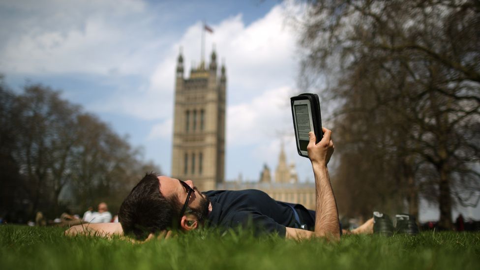 Man reads e-book on grass outside the Houses of Parliament