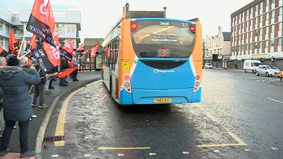 Striking bus drivers wave banners at the picket line as a Stagecoach bus is driven past