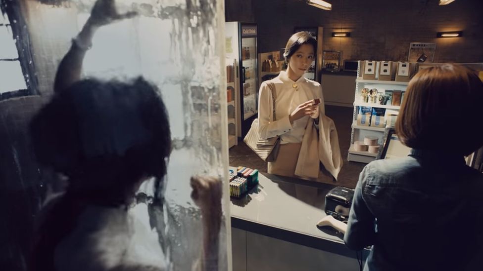 A still from the advert showing a woman trapped inside a packet, watching herself buy cigarettes