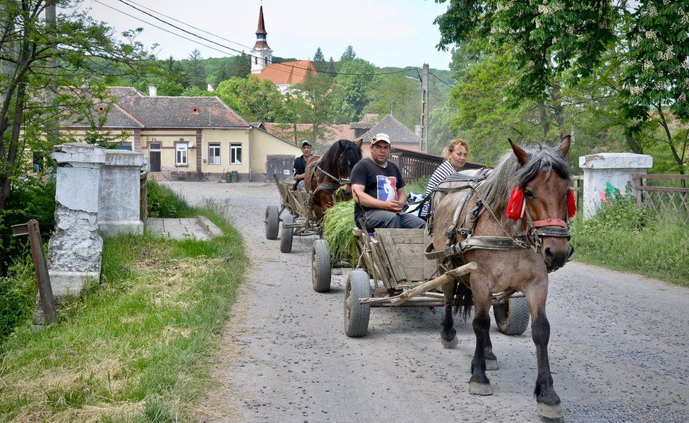 People ride on a horse and carriage carrying hay