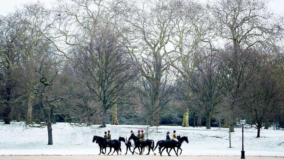 A group of horses and riders walk through a snow-covered Hyde Park