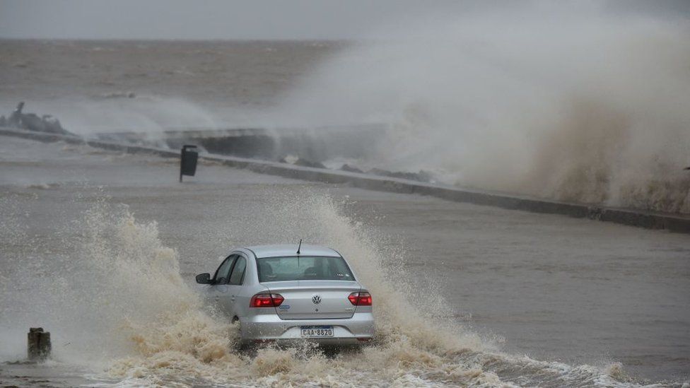 A car drives along a flooded street as waves crash over Montevideo's Rambla during the passage of a subtropical cyclone on May 17, 2022.