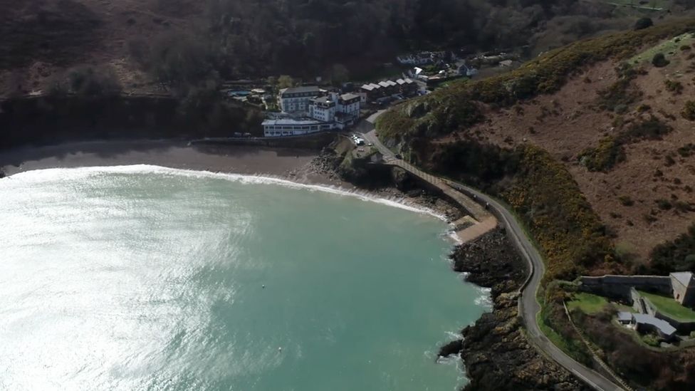 a high up shot of bouley bay - the sea beside a road and lots of woodland