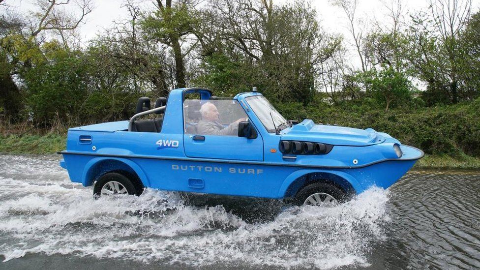 A blue amphibious car drives through flood water