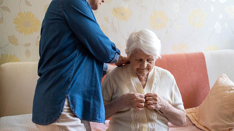 A carer helps an older woman dress