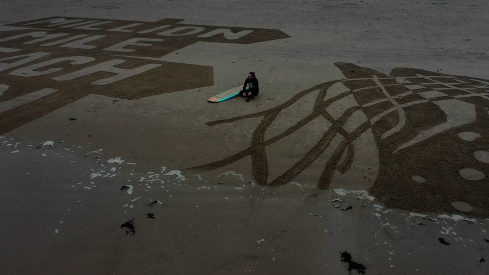 Surfer sitting on Cayton Bay beach between the sand drawing