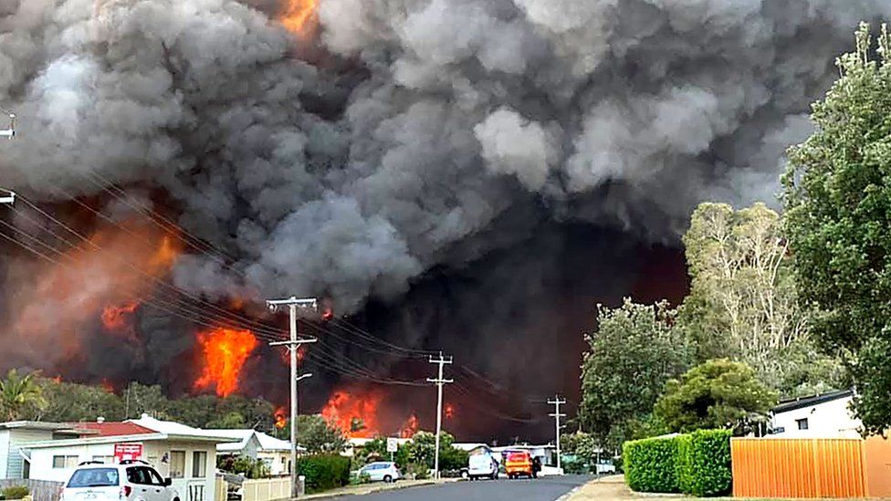 Massive flames and smoke clouds from a major bushfire hang over a suburban street in Harrington, New South Wales