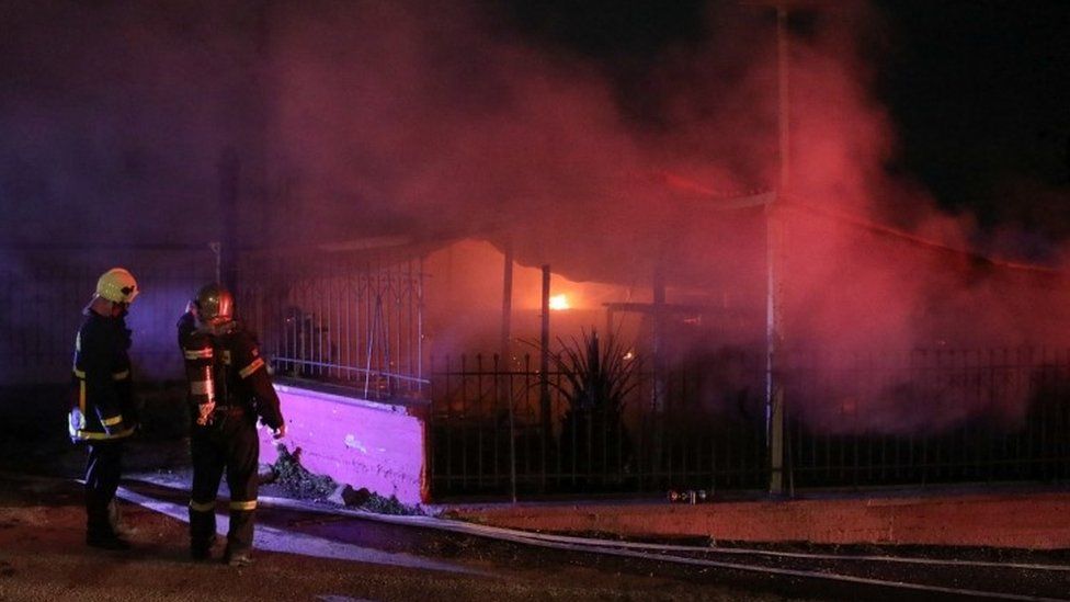 Firefighters stand next to the burning premises of a refugee centre on the island of Lesbos, Greece