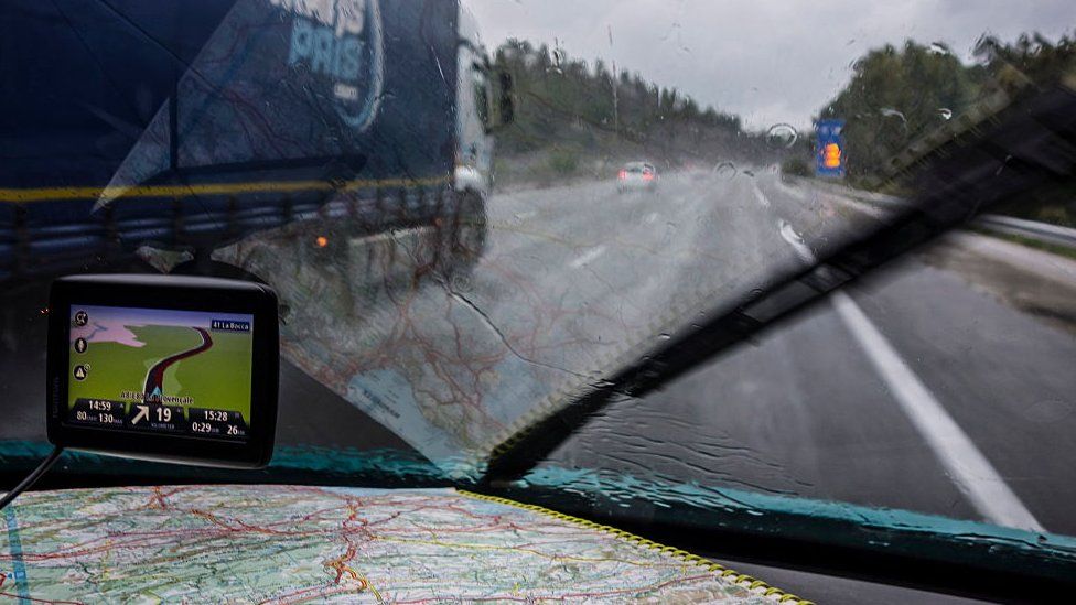 Speeding truck overtaking car on highway during heavy rain shower seen from inside of vehicle with GPS and road map on dashboard