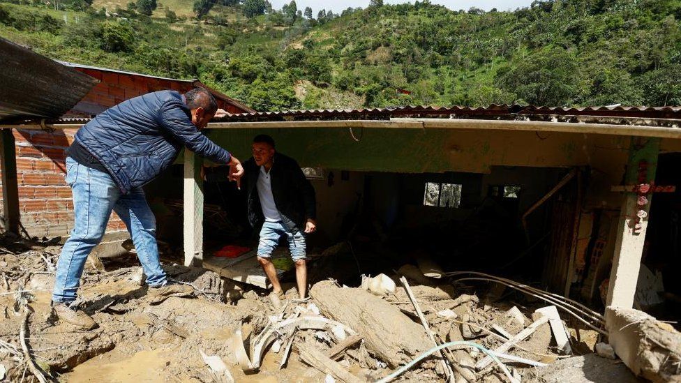Residents chat as they recover their belongings from a house damaged by a landslide which left several casualties and others injured, in Quetame, Colombia, July 18, 2023.