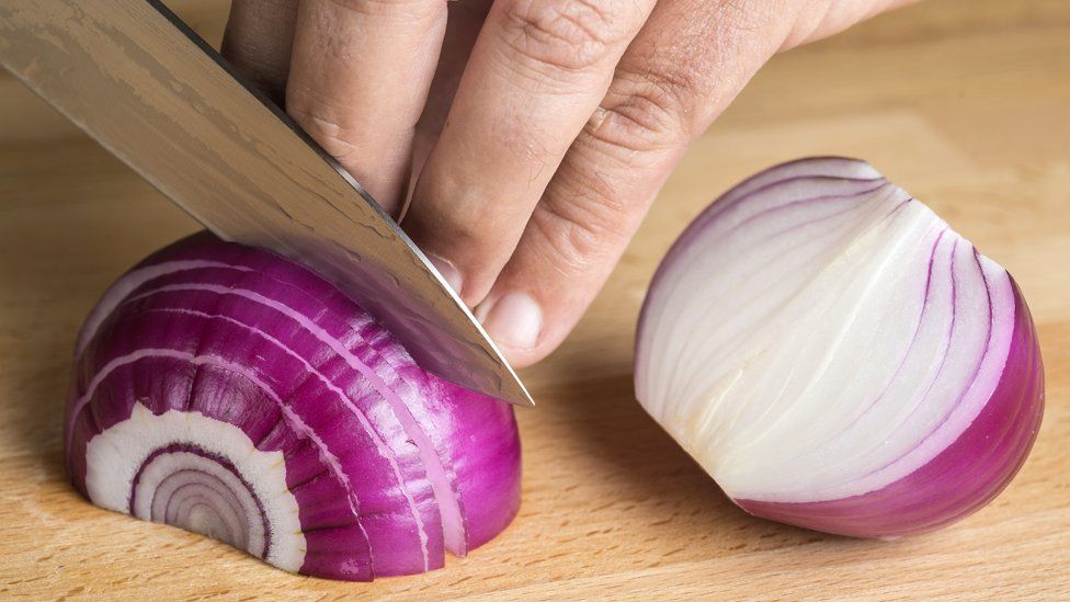 sharp knife slicing onion perilously close to some fingers