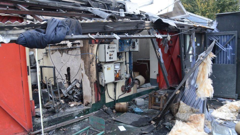 The aftermath of the explosion at Le Maitre Limited shows a missing wall and roof and torn materials and