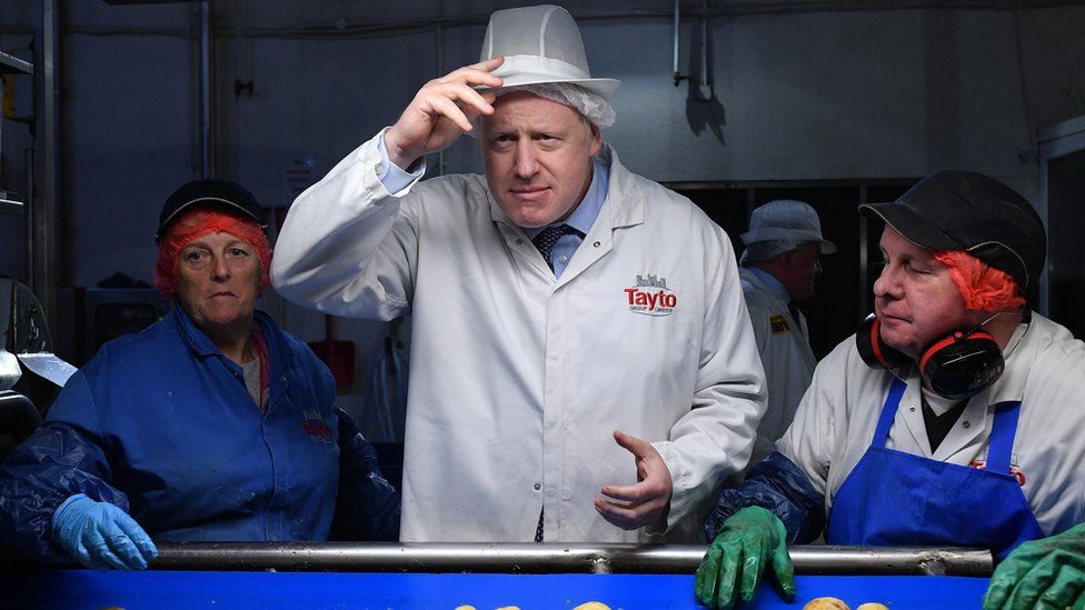 Boris Johnson on a visit to the Tayto factory, in a white jacket and workers hygiene hat